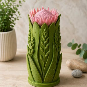 May include: A decorative vase featuring a pink protea flower design. The vase is green with detailed leaf and stem patterns. The flower has a textured, layered appearance. The vase is approximately 8 inches tall.
