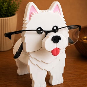 May include: A white dog-shaped spectacle holder with black-framed glasses. The holder features pink inner ears, a black nose, and a red tongue. The dog is on a wooden surface.