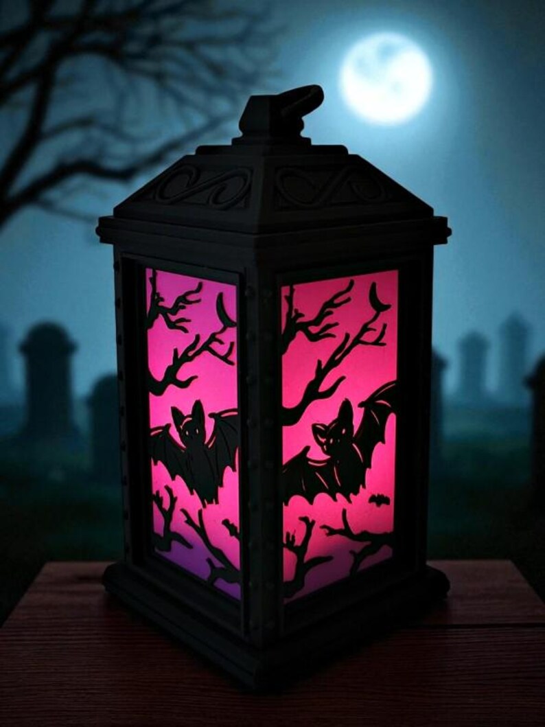 May include: A black Halloween lantern with a pink and purple illuminated interior. The lantern features bat and tree branch cutouts. The background shows a graveyard scene with a full moon.