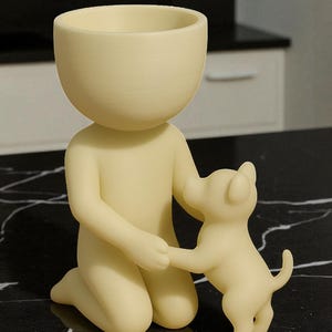K&ouml;nnte beinhalten: Cremefarbene Figur einer knienden Person, die die Pfote eines kleinen Hundes h&auml;lt. Der Kopf der Person ist eine gro&szlig;e, offene Schale. Der Hund steht auf seinen Hinterbeinen und blickt die Person an. Die Figur steht auf einer schwarzen Oberfl&auml;che.