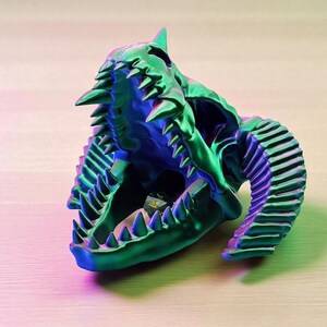 Op de afbeelding: Een 3D-geprinte schedelsculptuur in groen en blauw met een open mond en scherpe tanden. De sculptuur heeft een getextureerd oppervlak en is waarschijnlijk een decoratief item.