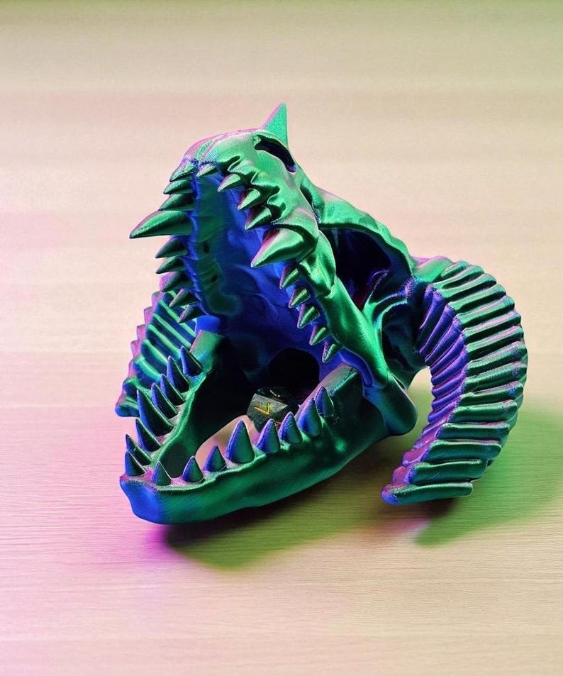 Op de afbeelding: Een 3D-geprinte schedelsculptuur in groen en blauw met een open mond en scherpe tanden. De sculptuur heeft een getextureerd oppervlak en is waarschijnlijk een decoratief item.