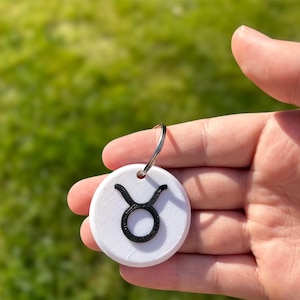 May include: White keyring with a black Taurus zodiac symbol.