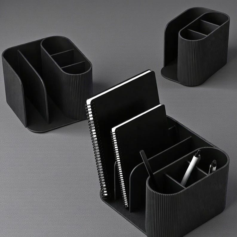 May include: Black desk organizers with multiple compartments and a ribbed texture. The organizers hold notebooks and pens. The design is modern and minimalist, suitable for office or home use.
