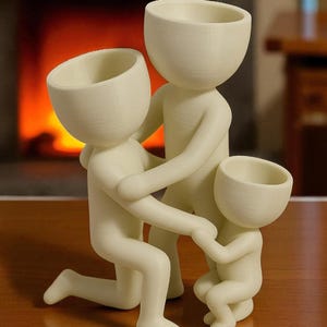 Op de afbeelding: Een cr&egrave;mekleurig familiebeeldje. De sculptuur toont een knielende figuur, een staande figuur en een kleinere zittende figuur, allemaal met open hoofdvormen. De figuren zijn in elkaar verweven, wat een gezinseenheid suggereert. De achtergrond toont een open haard.