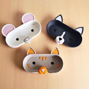 Pode incluir: Tr&ecirc;s bandejas em forma de animais: um rato branco com orelhas cor-de-rosa, um gato preto com orelhas brancas e um gato cinzento com orelhas laranja. Cada bandeja tem formato oval, ideal para guardar pequenos objetos.