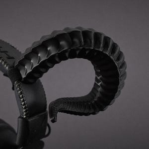 May include: Black headphones featuring a distinctive, curved horn-shaped design. The headphones have a padded headband and earcups, with visible stitching. The horn-like structure is textured, adding a unique visual element.