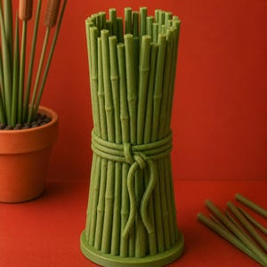 May include: A green bamboo-style vase with a bundle design. The vase is tied with a rope-like detail around the middle. The vase is cylindrical with a round base and is made of a solid green material. The background is a solid red.