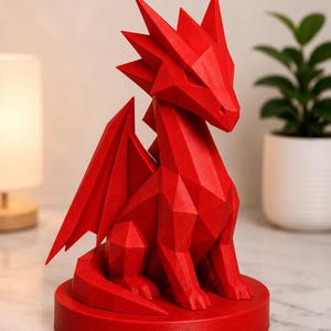 May include: A red, geometric dragon sculpture with sharp angles and a detailed design. The dragon has wings and is seated on a round base. The sculpture is a decorative item.