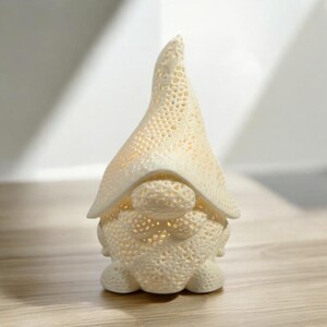 May include: A cream-colored gnome figurine with a pointed hat and round body. The gnome has a textured, perforated design, and the interior glows with a warm light. The figurine is a decorative item.