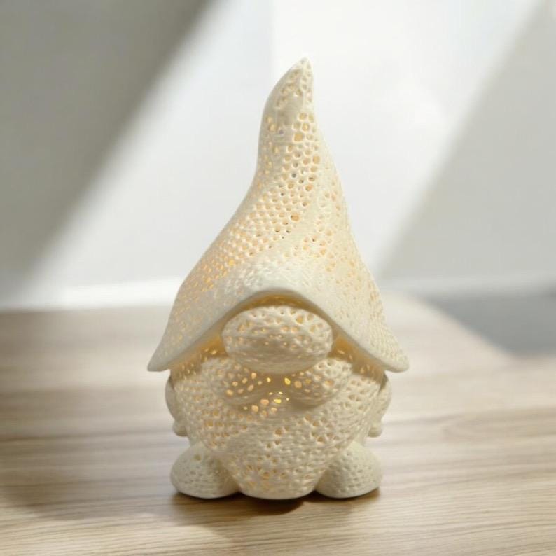 May include: A cream-colored gnome figurine with a pointed hat and round body. The gnome has a textured, perforated design, and the interior glows with a warm light. The figurine is a decorative item.