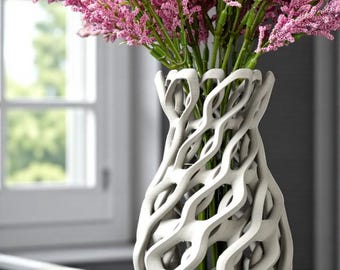May include: A white, intricately designed vase filled with vibrant pink flowers. The vase has a unique, openwork pattern, creating a modern and artistic look. The flowers are a bright pink, adding a pop of color to the neutral tones of the vase and background.