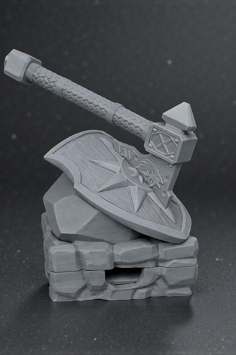 May include: A gray miniature axe and shield set, resting on a stone-like base. The axe features a textured handle and a detailed head. The shield displays a star and a wolf's head. This item is likely a collectible or decorative piece.