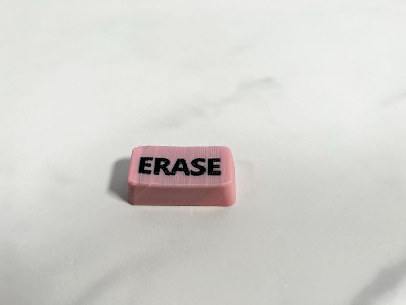 May include: A pink rectangular eraser with the word "ERASE" printed in black letters.