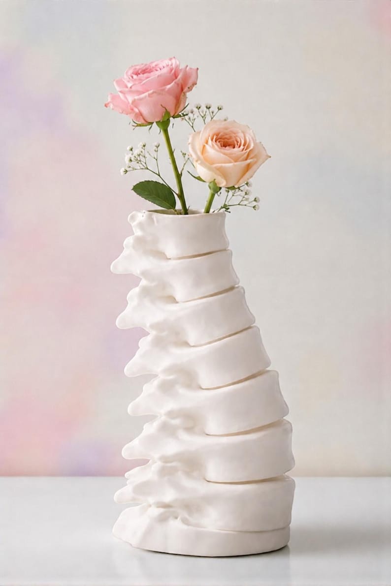 May include: A white ceramic vase shaped like a spine, holding two roses. One rose is light pink, the other is peach. The background is a soft gradient of pink, purple, and white.