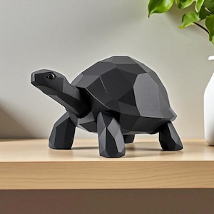 May include: A black geometric turtle sculpture with a faceted design. The decorative figurine is made of a solid material and is displayed on a light-colored wooden surface. The turtle has a detailed head, legs, and shell.