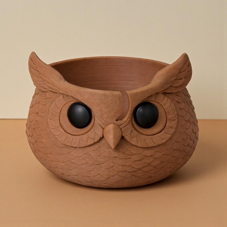 May include: A brown owl-shaped planter with large black eyes and detailed feather textures. The planter has a wide opening for plants and is made of a terracotta-like material. The owl's ears are prominent, adding to its whimsical design.
