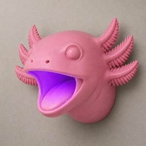 May include: A pink axolotl wall decor with an open mouth and a purple glow emanating from within. The axolotl has detailed gills and a smooth, matte finish. The design is mounted on a neutral-colored wall, creating a striking contrast.