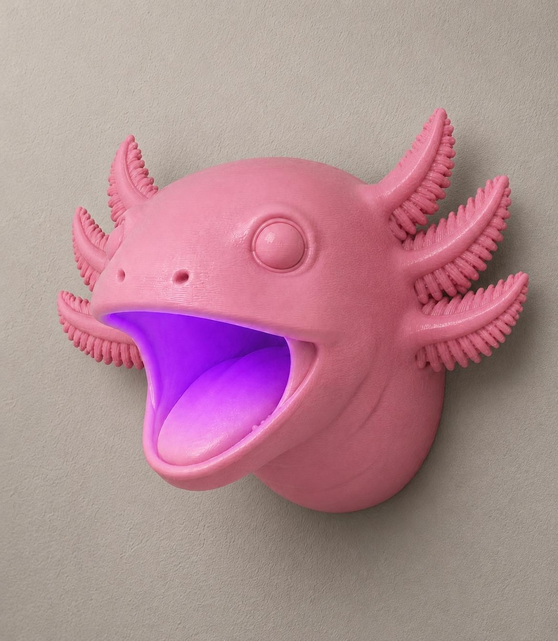 May include: A pink axolotl wall decor with an open mouth and a purple glow emanating from within. The axolotl has detailed gills and a smooth, matte finish. The design is mounted on a neutral-colored wall, creating a striking contrast.
