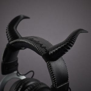 May include: Black leather headphones with a unique design featuring horns on the headband. The headphones have a stitched leather headband and earcups.