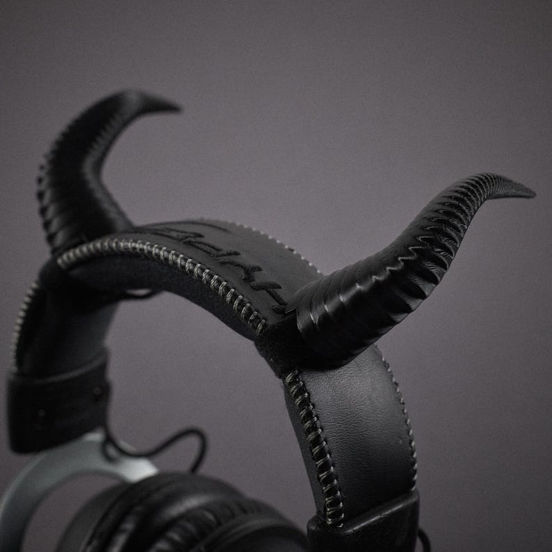 May include: Black leather headphones with a unique design featuring horns on the headband. The headphones have a stitched leather headband and earcups.