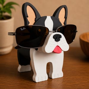 May include: A novelty sunglasses holder shaped like a French bulldog. The black and white dog has a red tongue and is wearing Ray-Ban sunglasses. The holder is made of wood and sits on a wooden surface.