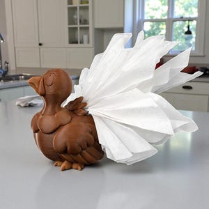 Puede incluir: Un servilletero marr&oacute;n con forma de p&aacute;jaro con un abanico de servilletas blancas. El soporte est&aacute; hecho de un material marr&oacute;n oscuro y tiene un dise&ntilde;o tallado detallado. Las servilletas est&aacute;n cuidadosamente dispuestas.