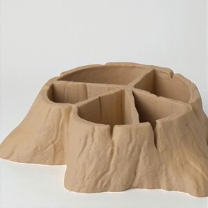 May include: A tan-colored, tree stump-shaped organizer with multiple compartments. The organizer has a textured surface resembling tree bark. The compartments are divided by vertical walls, creating separate storage spaces. The overall design is natural and rustic.
