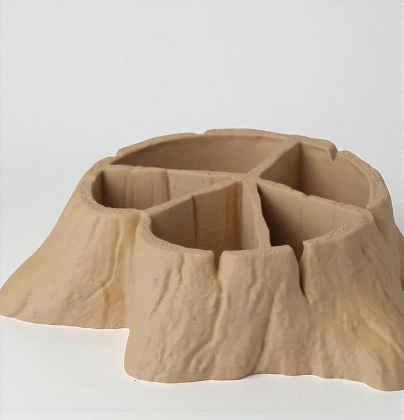 May include: A tan-colored, tree stump-shaped organizer with multiple compartments. The organizer has a textured surface resembling tree bark. The compartments are divided by vertical walls, creating separate storage spaces. The overall design is natural and rustic.