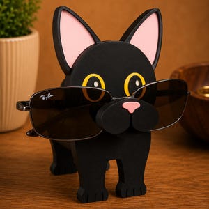 May include: A black wooden dog-shaped eyeglass holder with pink ears and a pink nose. The dog is wearing a pair of sunglasses with dark lenses. The holder is on a wooden surface.