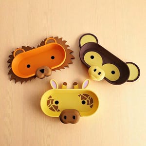 Puede incluir: Tres bandejas con forma de animales: un le&oacute;n, un mono y una jirafa. El le&oacute;n es naranja con una melena marr&oacute;n, el mono es marr&oacute;n con detalles amarillos y la jirafa es amarilla con manchas marrones. Cada bandeja tiene un dise&ntilde;o de cara.