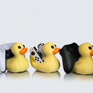 May include: A row of yellow rubber duck figurines, each holding a different video game controller. The controllers are white, black, and a combination of white and black. The ducks have orange beaks and black eyes.