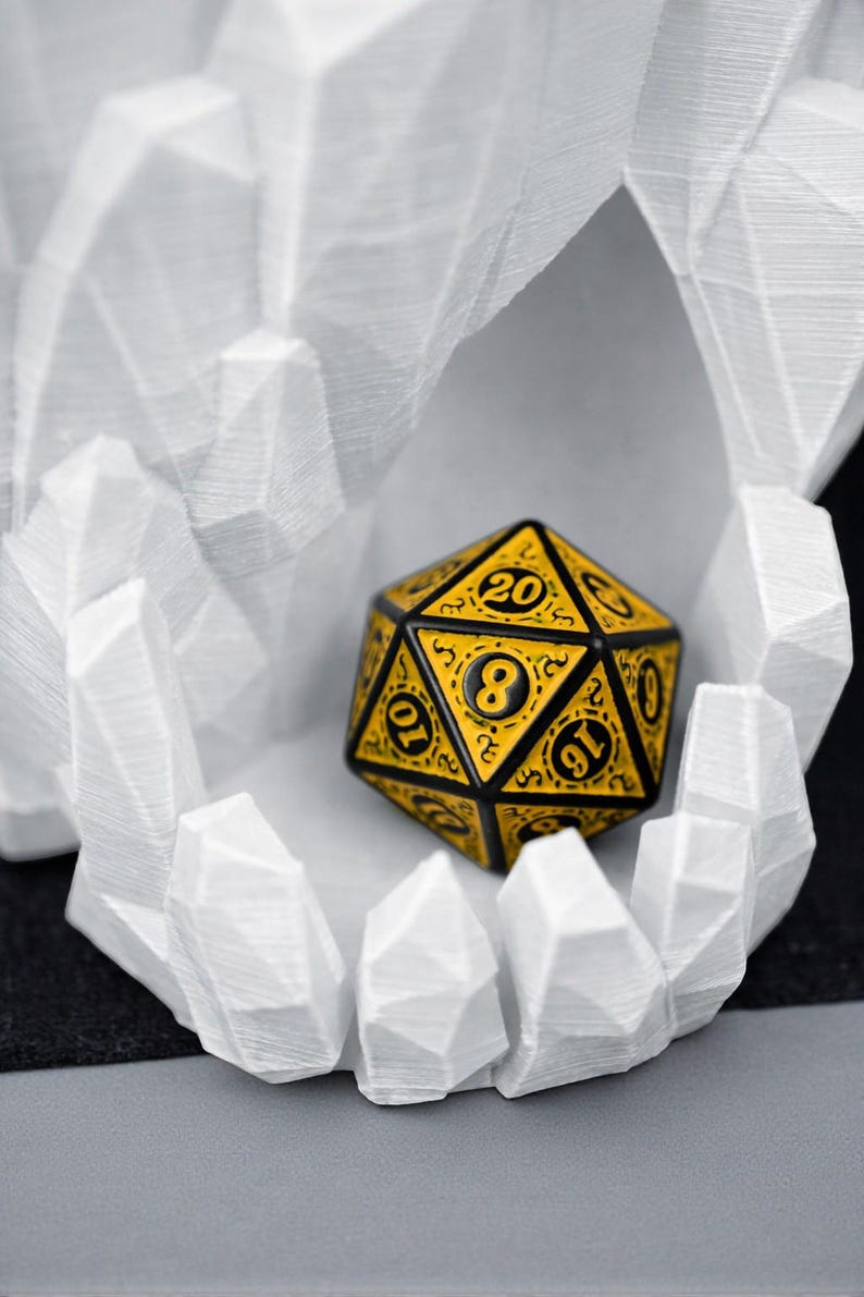 May include: A yellow and black twenty-sided die, with numbers and decorative patterns, rests inside a white, geometric, crystalline structure. The die is the focal point, showcasing its intricate design and the contrast between the colors.