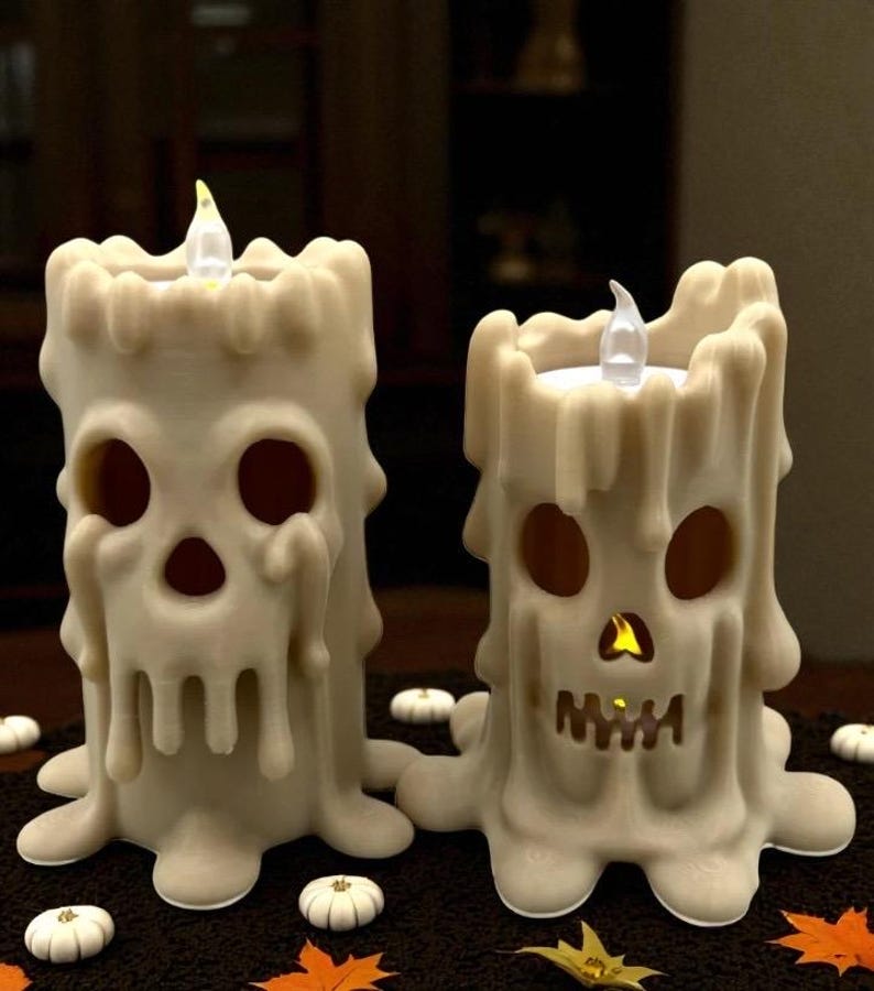May include: Two off-white Halloween-themed candle decorations. Each candle has a skull face design with eye and mouth cutouts. The candles have a melted wax appearance and are lit with a flickering LED light.