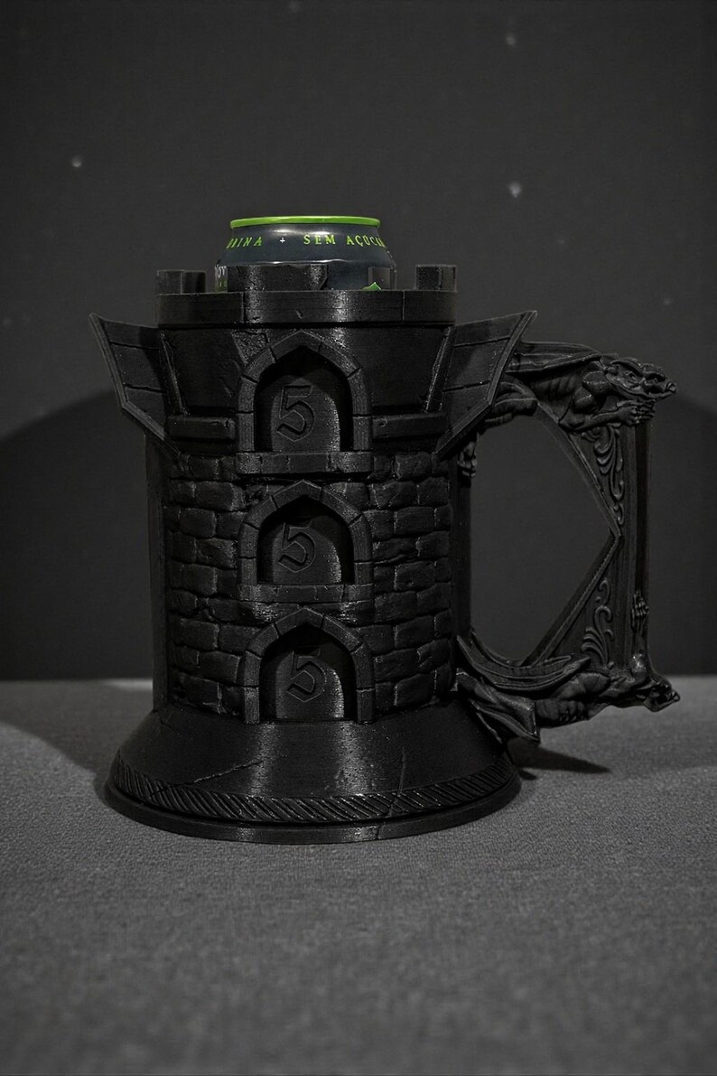 May include: Black castle-shaped mug with a handle featuring a dragon design. The mug has a cylindrical body with arched openings, each displaying the number "5". A green and silver can is inside the mug. The mug is made of a dark material.