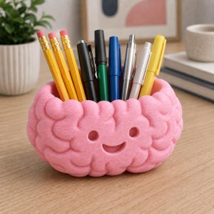 May include: A pink, brain-shaped desk organizer with a smiling face, holding a collection of various pens and yellow pencils. The container features a textured, convoluted surface resembling a human brain, providing a functional storage space.