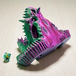 Op de afbeelding: Een 3D-geprinte, veelkleurige drakenkop met een gedetailleerd ontwerp. De schedel is voornamelijk groen en paars, met scherpe tanden en hoorns. Een kleine, veelkleurige dobbelsteen ligt naast de schedel. Het is een decoratief item.