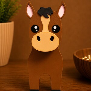 May include: A brown horse figurine with a white stripe down its face, large black eyes, and a tan muzzle. The horse has a black mane and hooves. The figurine is made of a sturdy material and stands upright on a wooden surface.