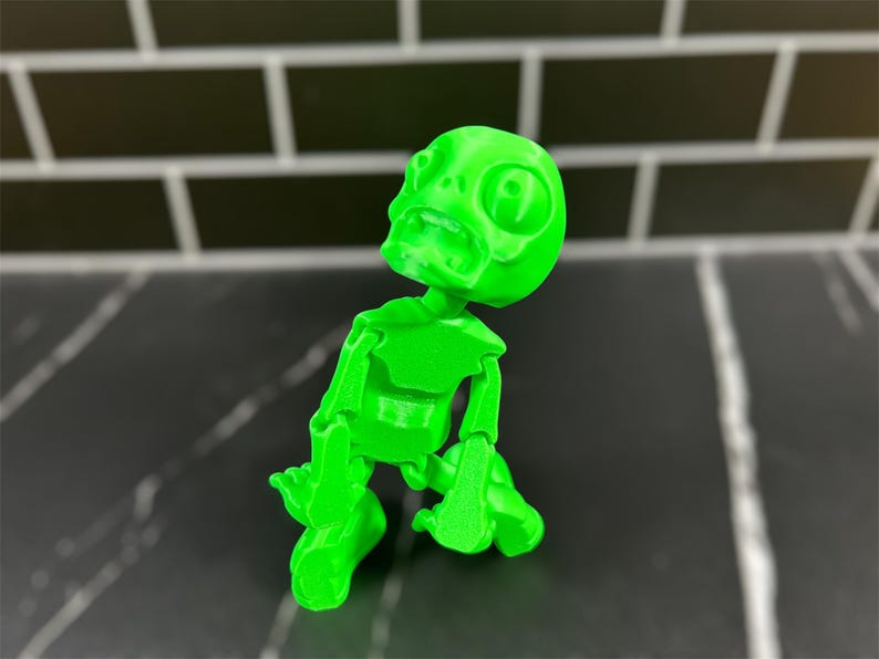 May include: A bright green 3D printed skeleton figurine with a comical expression. The skeleton is posed in a sitting position with its arms and legs bent.