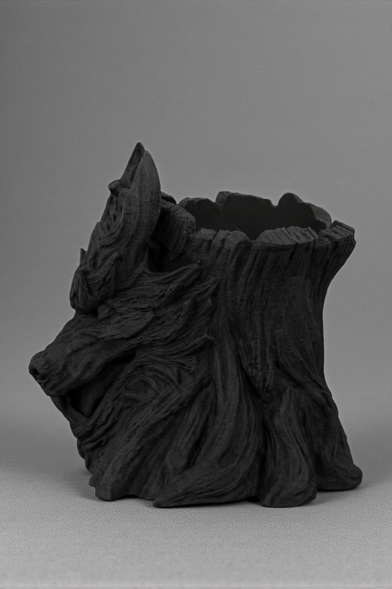 May include: A black, sculpted planter in the shape of a wolf's head. The planter has a textured surface, with detailed fur and facial features. The open top of the planter is visible, and the overall design is artistic and decorative.