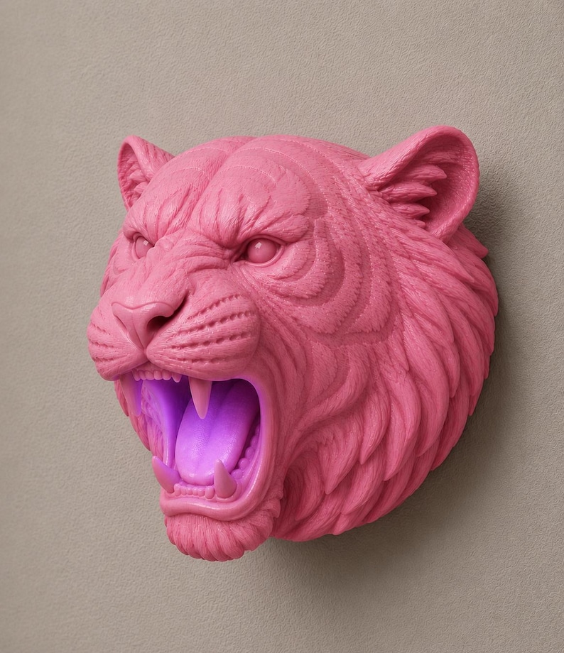 May include: A pink tiger head sculpture with an open mouth, revealing sharp teeth and a glowing purple interior. The sculpture is mounted on a neutral-toned wall, showcasing the detailed texture of the tiger's fur and facial features.