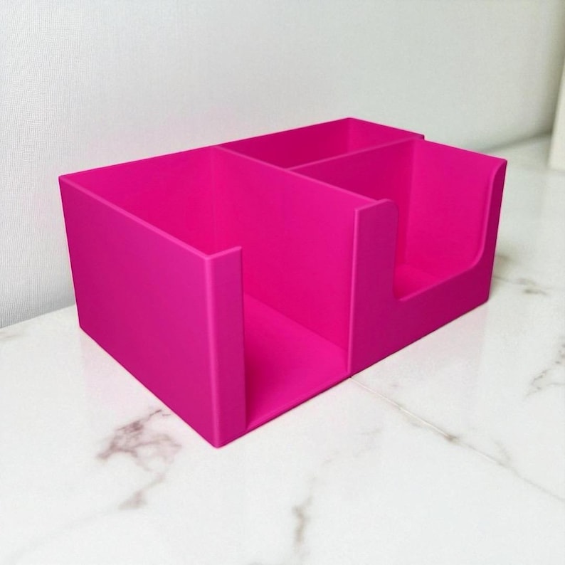 May include: A bright pink desk organizer with three compartments. The organizer is rectangular with a smooth, matte finish. The compartments are divided by vertical dividers, creating separate storage spaces for office supplies or other items.