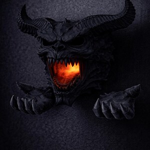 May include: A black, horned demon head sculpture with a fiery orange glow emanating from its open mouth. The sculpture has sharp teeth and outstretched hands, creating a menacing and detailed appearance. The background is a dark, textured surface.