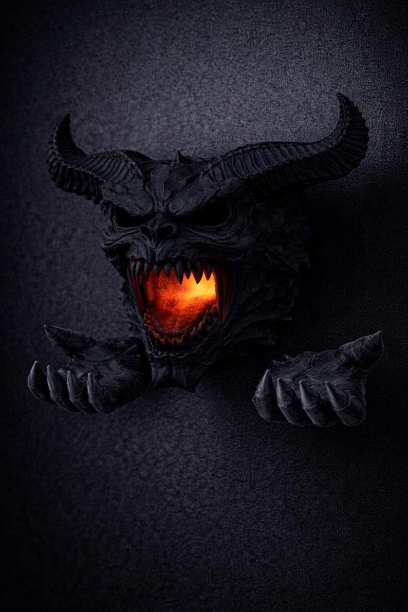 May include: A black, horned demon head sculpture with a fiery orange glow emanating from its open mouth. The sculpture has sharp teeth and outstretched hands, creating a menacing and detailed appearance. The background is a dark, textured surface.