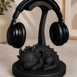 May include: Black headphone stand with a sleeping dragon figurine base. The stand holds a pair of black headphones. The dragon is black with small horns and wings. The stand is on a round base.