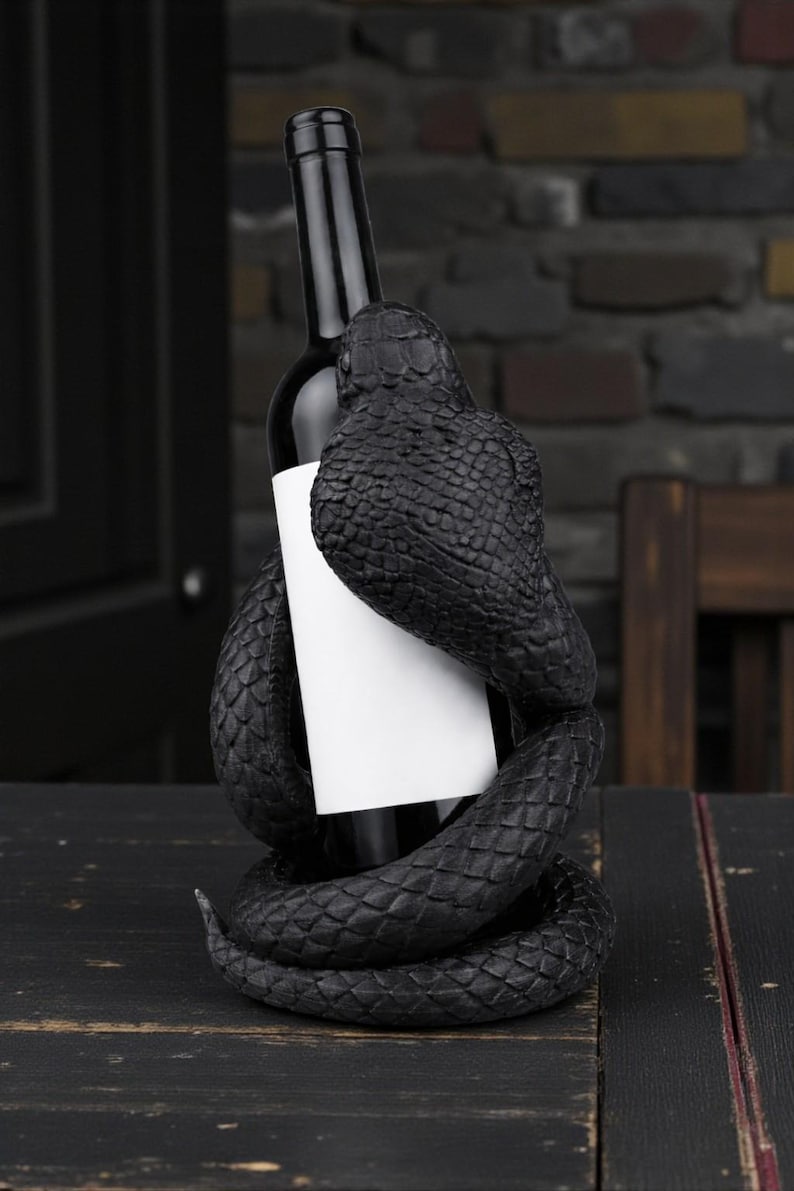 Puede incluir: Una botella de vino negra sujeta por un soporte decorativo de vino con forma de serpiente negra. El cuerpo de la serpiente se enrolla alrededor de la botella, creando una presentaci&oacute;n &uacute;nica y elegante. La botella tiene una etiqueta blanca.