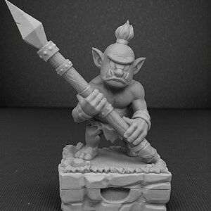 May include: A gray figurine of a goblin warrior holding a spear. The goblin is muscular, with a stern expression and a mohawk. It stands on a stone base, ready for battle. The spear is detailed with a pointed tip and a wooden shaft.