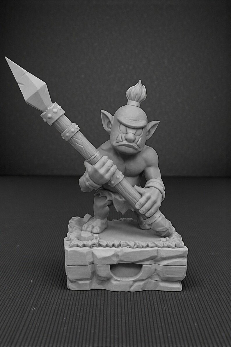 May include: A gray figurine of a goblin warrior holding a spear. The goblin is muscular, with a stern expression and a mohawk. It stands on a stone base, ready for battle. The spear is detailed with a pointed tip and a wooden shaft.