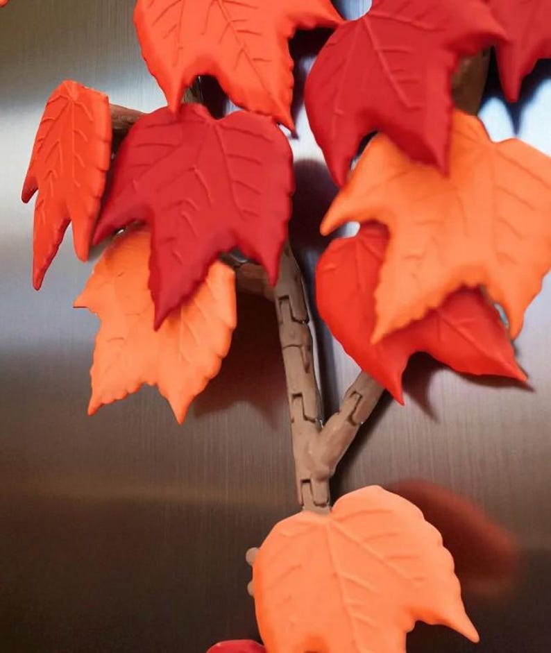 May include: A decorative fall-themed piece featuring a branch with vibrant, textured leaves. The leaves are in shades of red, orange, and yellow, creating a warm, autumnal aesthetic. The branch is a light brown color.