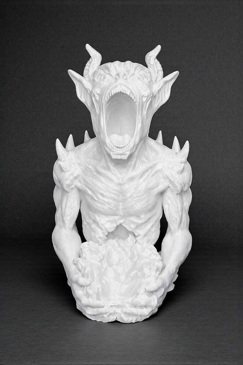 May include: A white sculpture of a demonic creature with an open mouth, horns, and sharp protrusions. The figure is holding a textured mass in its hands, set against a dark background. The sculpture has a detailed, textured surface.